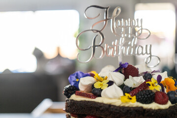 Decorated chocolate cake with berries, flowers, meringue and cream With happy birthday sign