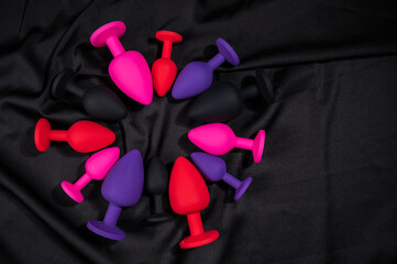A set of silicone anal plugs in different colors and sizes on a black silk sheet. 