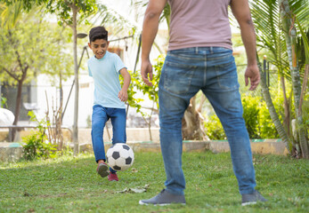 Close shot of father and son playing with football at park - concept of summer holidays, relationship and active lifestyle.