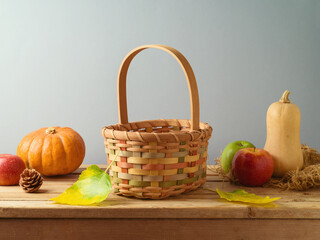 Empty basket with pumpkin and apples on wooden table over gray background. Autumn and Thanksgiving...