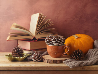 Autumn concept with pine cone in coffee cup, pumpkin and books on wooden table. Thanksgiving greeting card