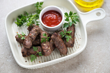 Grilled serbian cevapi or cevapcici with fresh parsley and dip in a beige serving tray, horizontal shot, middle close-up