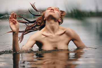 Naked woman tossing hair in a lake - 618824154