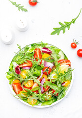 Fresh vegan vegetable salad with colorful tomatoes, cucumber, red onion, lettuce and arugula. White table background, top view