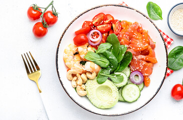 Keto salad with spinach, salmon, shrimp, avocado, cucumber, tomato, nuts, sesame seeds. Low-carbohydrate lunch rich in healthy fats. White table background, top view