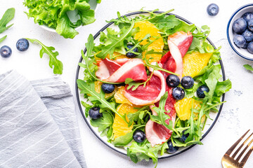 Gourmet duck salad with smoked breast and orange, blueberry lettuce and arugula leaves on white table background, top view