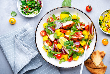 Fresh salad with grilled chicken and mango, salsa, tomatoes, cilantro, red onion and lettuce in tex-mex style, white table background, top view