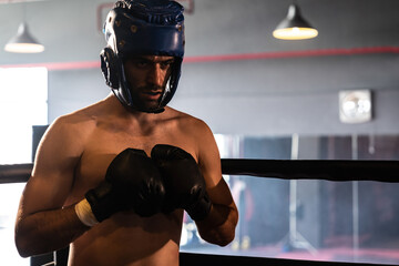Boxing fighter with head guard posing, caucasian boxer punch his fist in front of camera in aggressive stance and ready to fight at the boxing match ring. Impetus
