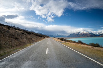 Scenic view at Mount Cook Road alongside Lake Pukaki with snow capped Southern Alps basking in the late winter evening light. Best road trip route in New Zealand South Island.