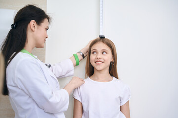 Pediatrician measuring little girl height with special tool