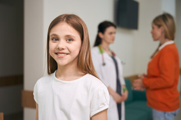 Happy girl patient of pediatrician clinic looking at camera and smiling - obrazy, fototapety, plakaty