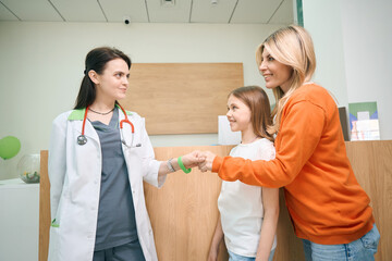Mother shaking hand to pediatrician of her little daughter - obrazy, fototapety, plakaty