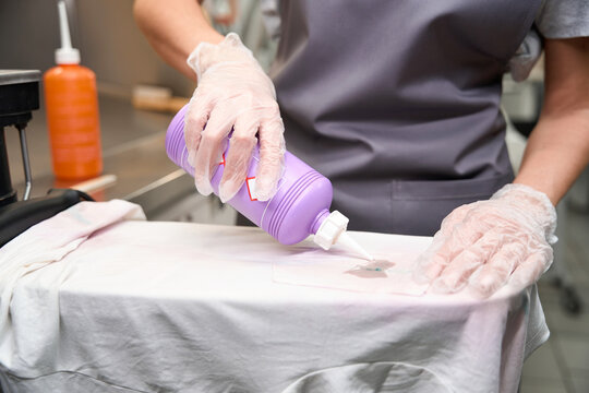 Woman in protective gloves applying solvent into spot on t-shirt