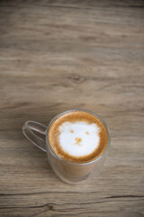 A hot latte with milk froth painted in the shape of a bear's face on wood table