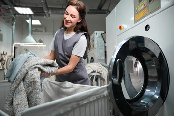 Dry cleaning service worker loading industrial washing machine with clothes