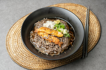 A summer dish of cold wheat noodles with fried shrimp in a black bowl