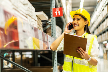 Asian woman in helmet and uniform talks on mobile phone discuss amount of stock product inventory on shelf at distribution warehouse factory. logistic business shipping and delivery service