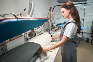 Dry cleaning service operator putting coat on pressing machine