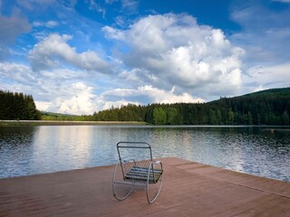 Rocking chair on a wooden pontoon near the lake on a cloudy summer day
