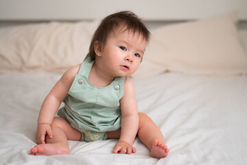 Fototapeta premium Mixed ethnicity Asian Caucasian 8 months baby girl - lifestyle home portrait of adorable and happy female child lying playful on bed exploring the surroundings curious