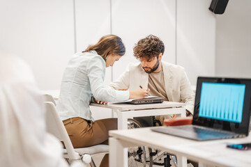 Obraz premium Handicapped male employee in wheelchair working together with his brunette female coworker