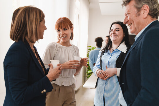 Diverse Colleagues Interacting During Office Break - Group of formal colleagues conversing and laughing in a modern office.