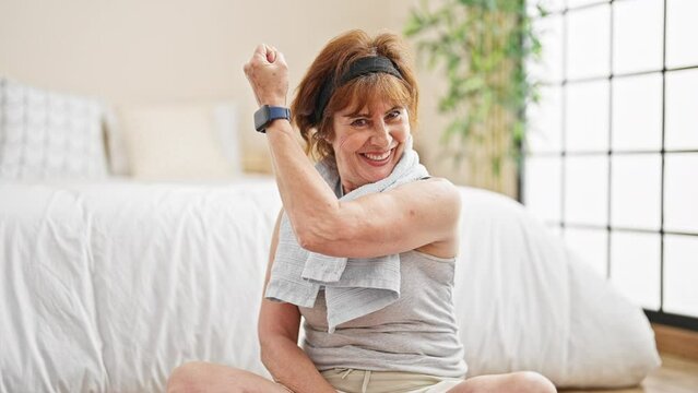 Middle age woman sitting on floor doing strong gesture with arm at bedroom