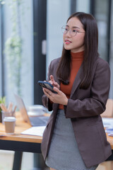 Sharing good business news. Attractive young businesswoman talking on the mobile phone and smiling while sitting at her working place in office and looking at laptop PC.