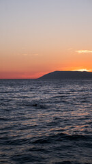 Ocean small waves on sunset lights.
Sun sitting  over the island. Beautiful view from evening beach.