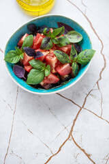 Bowl of tomato salad with balsamic sauce and fresh basil leaves, vertical shot on a white granite background with space, elevated view