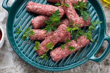 Green serving tray with raw cevapcici or skinless beef balkan sausages, middle close-up, selective focus, horizontal shot