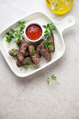 Beige serving tray with bbq serbian cevapi or cevapcici, fresh parsley and dip, above view on a beige stone background, vertical shot with space