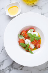 White plate with italian caprese salad, vertical shot on a white marble background, high angle view