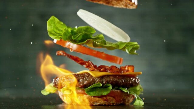 Super slow motion of stacking cheeseburger pieces. Camera in motion. Filmed on high speed cinema camera, 1000 fps. Placed on high speed cine bot. Fire on background.