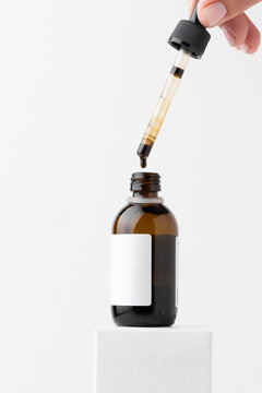 Woman dripping medical iodine from pipette into glass bottle on the white background. Close up of brown medicine liquid dripping into glass bottle. Potassium iodide for the thyroid gland medication
