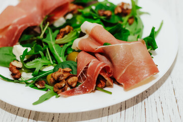 Salad with herbs, arugula, prosciutto, cheese, green olives and nuts.