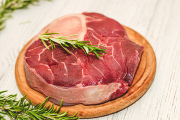 Fresh piece of meat large beef steak on the bone ossobuco with rosemary sprig.