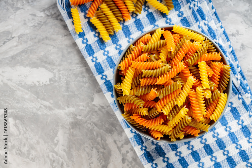 Wall mural Tricolor fusilli pasta in bowl on a gray background. Fusilli dry pasta on a linen napkin. Copy space