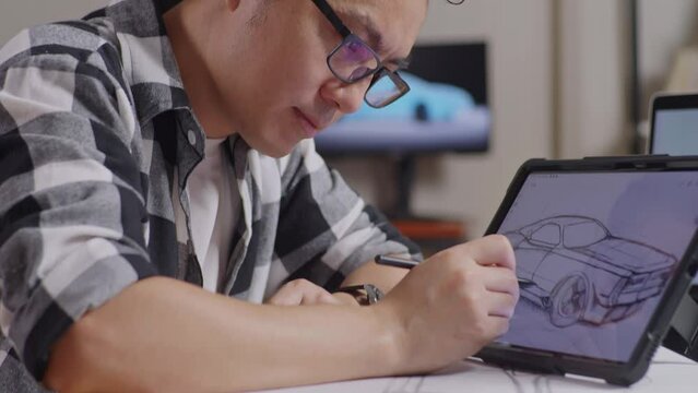 Close Up Of Asian Male Smiling To The Camera While Drawing New Car Design Concept On A Tablet In The Studio With Tv And Computers Display 3D Electric Car Model 
