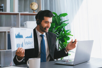 Business man wearing headphone present financial data or BI paper via laptop during online meeting. Remote work concept with virtual meeting presentation of effectiveness remote work. Fervent