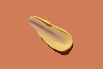 Yellow cosmetic smear of cream texture on a coral background. Skin care. Copy space.