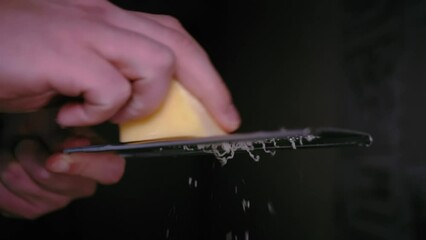 Slow Motion Video of a Skillful Hand Grating Cheese on a Fine Grater, Creating Finely Shredded Fresh Dairy Product with Precise and Delicate Movements