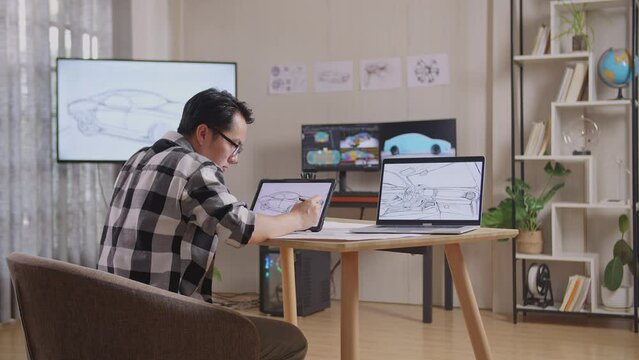Side View Of Asian Male Drawing New Car Design Concept On A Tablet In The Studio With Tv And Computers Display 3D Electric Car Model 
