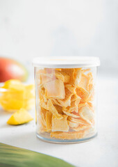 Freeze dried mangoes for cereal in plastic jar on light background.