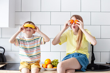 Happy children playing with fruits sitting in modern kitchen. Healthy food, good nutrition for kids concept. Selective focus.
