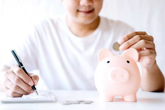 A young man was happy to use a coin to put a piggy bank into a piggy bank and take notes. concept of saving money for investment