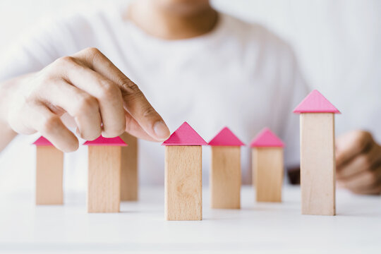 Hands of young man assembling house model from wooden blocks, village construction concept from wooden blocks and planning concept saving money to buy a house