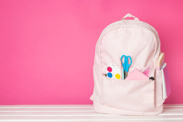 Pink school backpack with stationery on wooden table