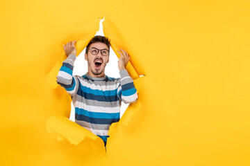 front view shouting young man looking through ripped paper yellow wall