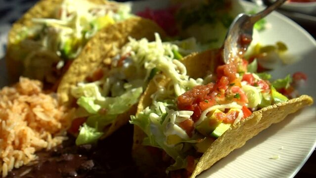 Spoon adding spicy chilli salsa to hard shell corn taco pork cheese and lettuce Mexican delicious food
